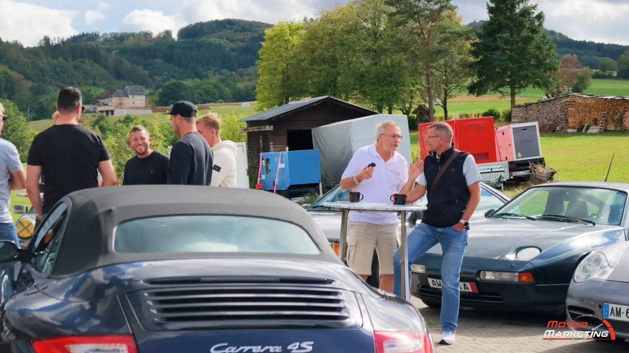 Gäste mit Kaffee zwischen Porsche Modellen in der Eifellandschaft